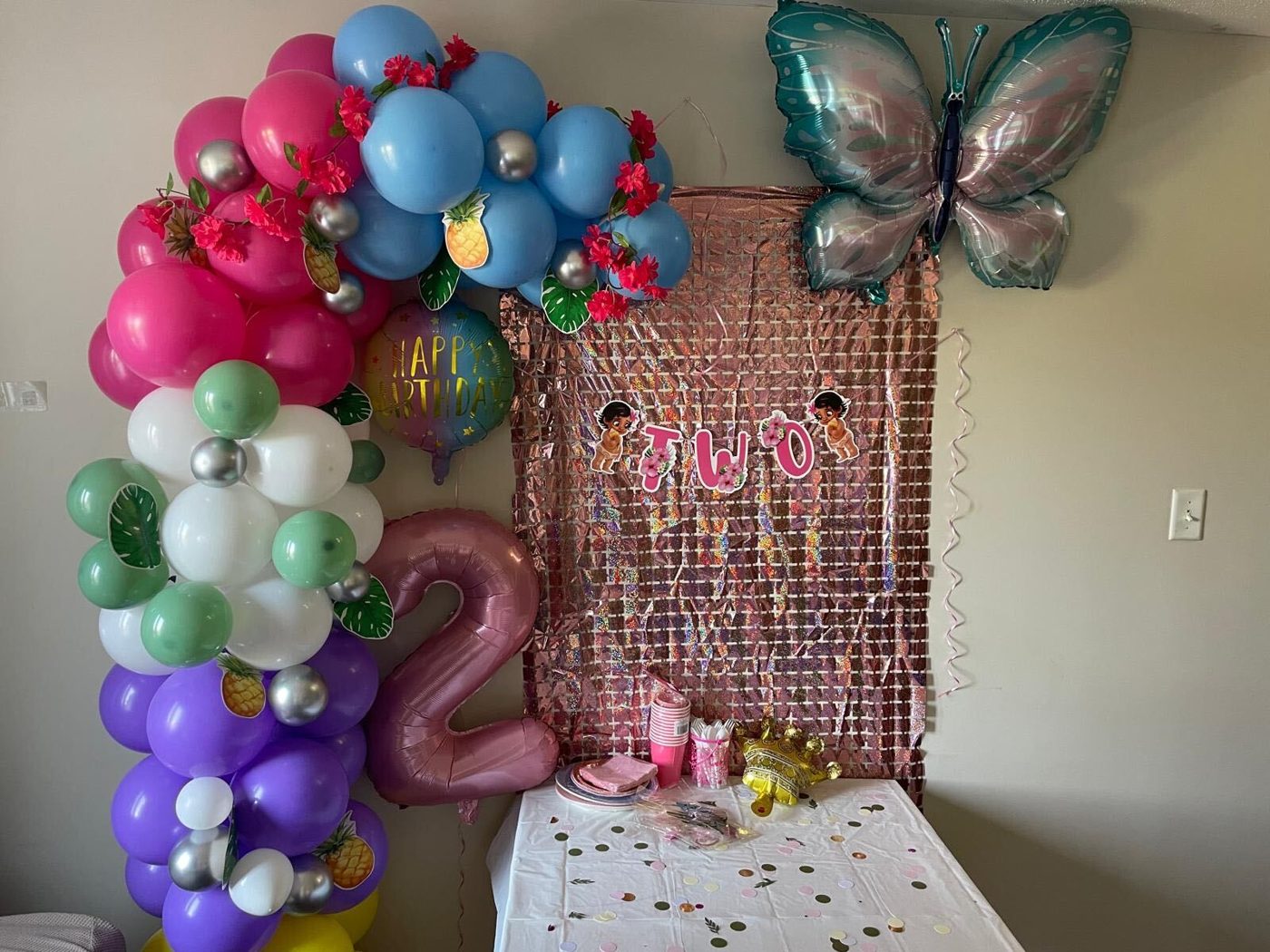 Tropical second birthday with balloon garland, pineapple accents, butterfly balloon and a rose shimmer wall